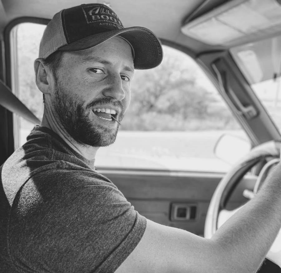 Alex Starr in a trucker hat, driving a truck